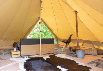 Interno di una tenda glamping con tappeti, pelle, seduta e decorazioni rustiche in una zona naturale.