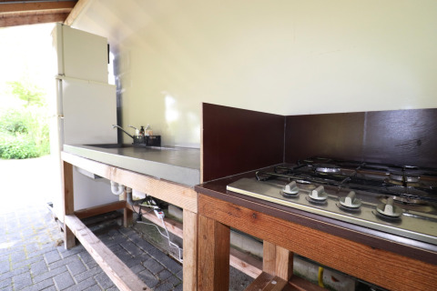 Udendørs glampingkøkken med gaskomfur, håndvask og køleskab, velegnet til komfortabel madlavning.
