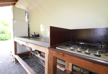 Outdoor glamping kitchen with gas stove, sink, and refrigerator, perfect for comfortable cooking.
