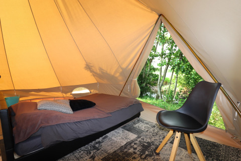 Indretningen indeni et glamping-telt med en enkeltseng, stol og udsigt til grøn vegetation udenfor.
