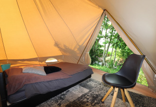 Interno di una tenda glamping con letto singolo, sedia e finestra che mostra alberi verdi all’esterno.