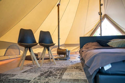 Innenansicht einer Glamping-Unterkunft mit stilvollen Stühlen, Bett und Holzofen im großen Zelt.