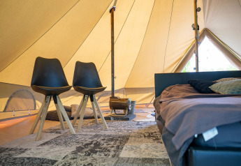 Intérieur d'une tente glamping avec un lit confortable, des chaises modernes et un poêle à bois.