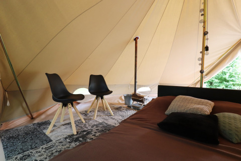 Interno di una tenda glamping con due sedie nere, letto con cuscini e tappeto elegante.