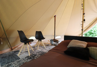 Indrettet telt med to sorte stole, seng med puder og tæppe på gulvet i glamping-indkvartering.
