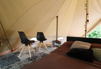 Intérieur de tente glamping avec deux chaises noires, lit avec coussins et décoration chic au sol.