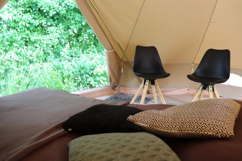 Vista interna di una tenda glamping con cuscini su un letto e due eleganti sedie nere vicine.