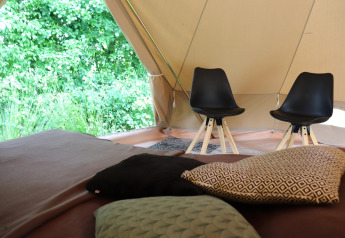 Vue intérieure d'une tente glamping avec des coussins sur un lit et deux chaises noires modernes à côté.