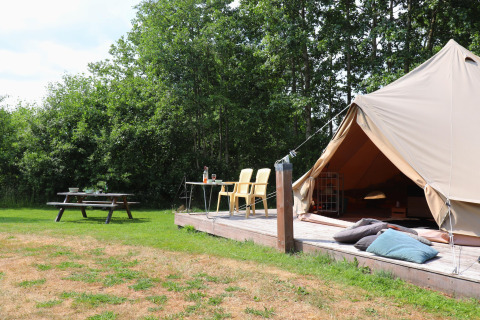 Glamping-indkvartering med telt på træterrasse, havestole, picnicbord og puder i naturskønne omgivelser.
