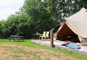Alloggio glamping con tenda su pedana in legno, sedie da giardino, tavolo da picnic e cuscini all’aperto.