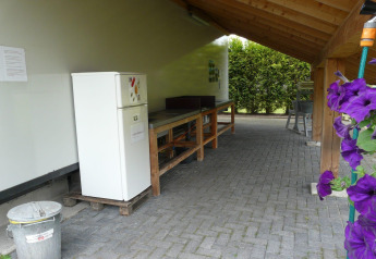 Cocina exterior en alojamiento glamping con nevera, banco de trabajo y flores violáceas al costado.