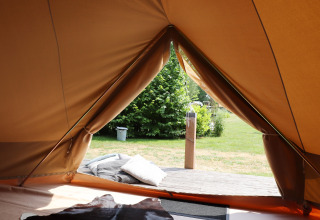Vista dall’interno di una tenda glamping verso una terrazza accogliente con cuscini e verde all’esterno.