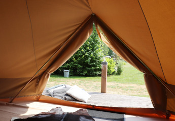 Vista dall’interno di una tenda glamping verso una terrazza accogliente con cuscini e verde all’esterno.