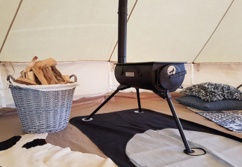 Cozy glamping tent interior featuring a wood-burning stove, firewood basket, and comfortable bedding.