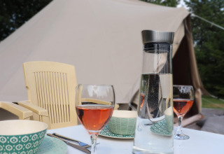 Glampingsetting met tafel, glazen roséwijn, een waterkaraf, kommen en een tent op de achtergrond.