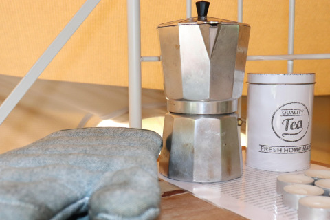 Una moka, una lattina da tè e una presina su un tavolo all'interno di una tenda glamping accogliente.