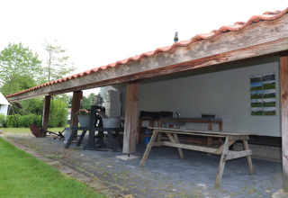 Cucina all’aperto e tavolo da picnic in legno sotto una veranda in un alloggio glamping verde.