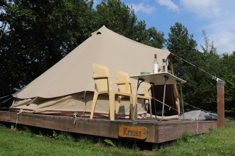 Tenda tipi glamour 'Kreas' nei Paesi Bassi, con due sedie gialle e un tavolo su una pedana di legno.