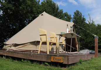 Tenda tipi glamour 'Kreas' nei Paesi Bassi, con due sedie gialle e un tavolo su una pedana di legno.