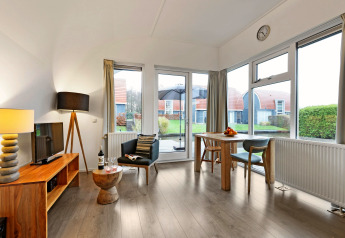 Lichte woonkamer in Water park De Bloemert 6 lodge met grote ramen, eettafel en uitzicht op de tuin.
