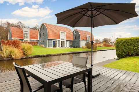 Terrazza sul canale al Water park De Bloemert 6, Paesi Bassi, con lodge moderni e grande ombrellone.