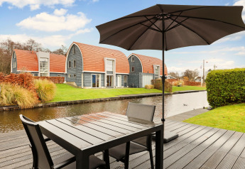Terrasse am Wasser im Water park De Bloemert 6, Niederlande, mit modernen Ferienhäusern und Sonnenschirm.