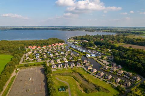 Vue aérienne d'un lodge sur le lac, entouré de villas modernes, arbres et paysages verdoyants.