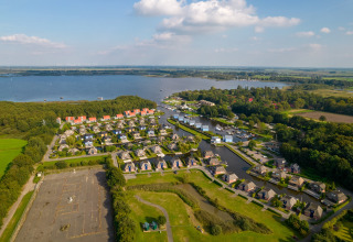 Luftfoto af et luksuriøst lodge-område omgivet af smuk natur, sø og grønne marker i solen.
