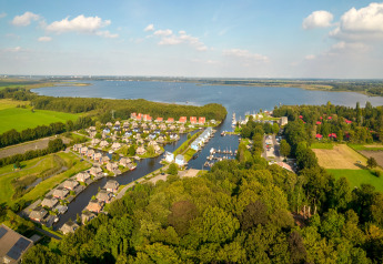 Veduta aerea di un lodge sul lago circondato da case, campi verdi, boschi e acqua blu tranquilla.