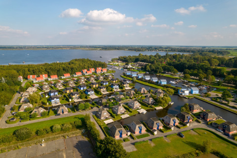 Vista aerea di un villaggio di lodge vacanza con canali d’acqua, vicino a un lago e foreste verdi.