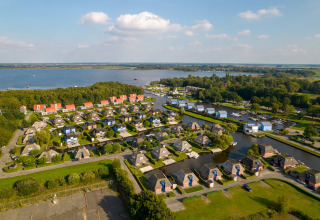 Aerial view of a scenic holiday lodge village with water channels, near a lake and lush green forests.