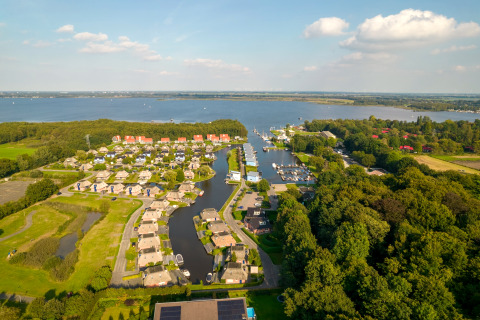 Luftaufnahme einer malerischen Lodge am See mit Ferienhäusern, viel Grün und Bootsanlegern im Hafen.