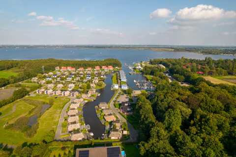 Luftfoto af en charmerende lodge ved søen, omgivet af hytter, grønne områder og både ved marinaen.