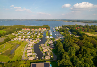 Vista aérea de una encantadora posada junto al lago, rodeada de cabañas, zona verde y barcos en el puerto.