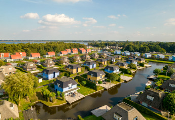 Vista aerea di un resort con lodge colorati, canali e barche vicino a un lago e a zone verdi.