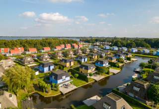 Vue aérienne d’un complexe de lodges colorés avec canaux, bateaux, proche d’un lac et de la forêt.