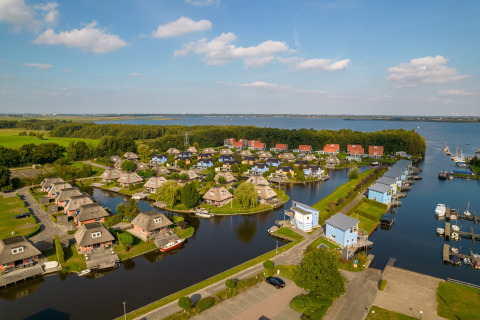 Luftfoto af en ferielodge med små hytter ved vandet, omgivet af grønt og med udsigt til en sø.