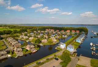 Luftbild einer Ferienanlage mit kleinen Häusern am Wasser, umgeben von grüner Natur und einem See.