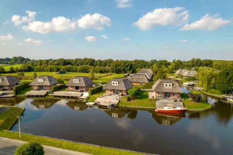 Luftaufnahme von Ferienhäusern am Wasser mit grüner Landschaft und blauem Himmel im Hintergrund.