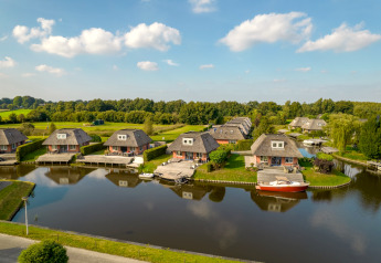 Luftaufnahme von Ferienhäusern am Wasser mit grüner Landschaft und blauem Himmel im Hintergrund.