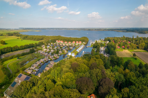 Vista aerea di un lodge sul lago circondato da campi verdi, boschi e case vicino all’acqua.