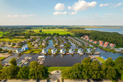 Vista aérea de un moderno complejo de cabañas junto al lago, puerto deportivo y entorno verde.