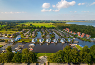 Vista aérea de un moderno complejo de cabañas junto al lago, puerto deportivo y entorno verde.