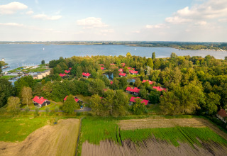 Vista aerea di un tranquillo lodge sul lago, circondato da alberi e campi, con casette dai tetti rossi.