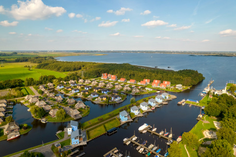 Vista aerea di un lodge sul lago con case moderne, pontili per barche e tanto verde attorno al paesaggio.