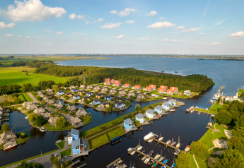 Vista aerea di un lodge sul lago con case moderne, pontili per barche e tanto verde attorno al paesaggio.