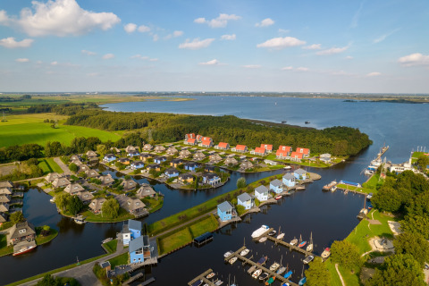 Vista aerea di un lodge sul lago con case moderne, pontili per barche e tanto verde attorno al paesaggio.