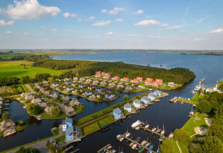 Aerial view of a lakeside lodge with modern houses, boat docks, and lush greenery under a blue sky.
