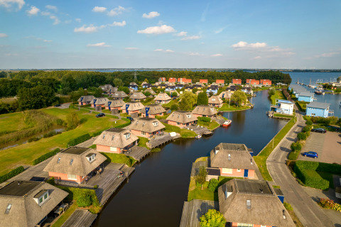 Luftaufnahme von Ferienhäusern an einem ruhigen Kanal mit Stegen, Rasenflächen und kleinen Booten.