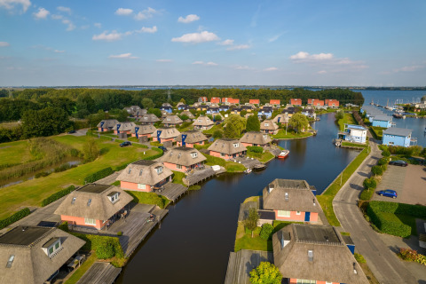 Luftfoto af hyggelige hytter ved en kanal, omgivet af grønne områder og både i et ferieanlæg.